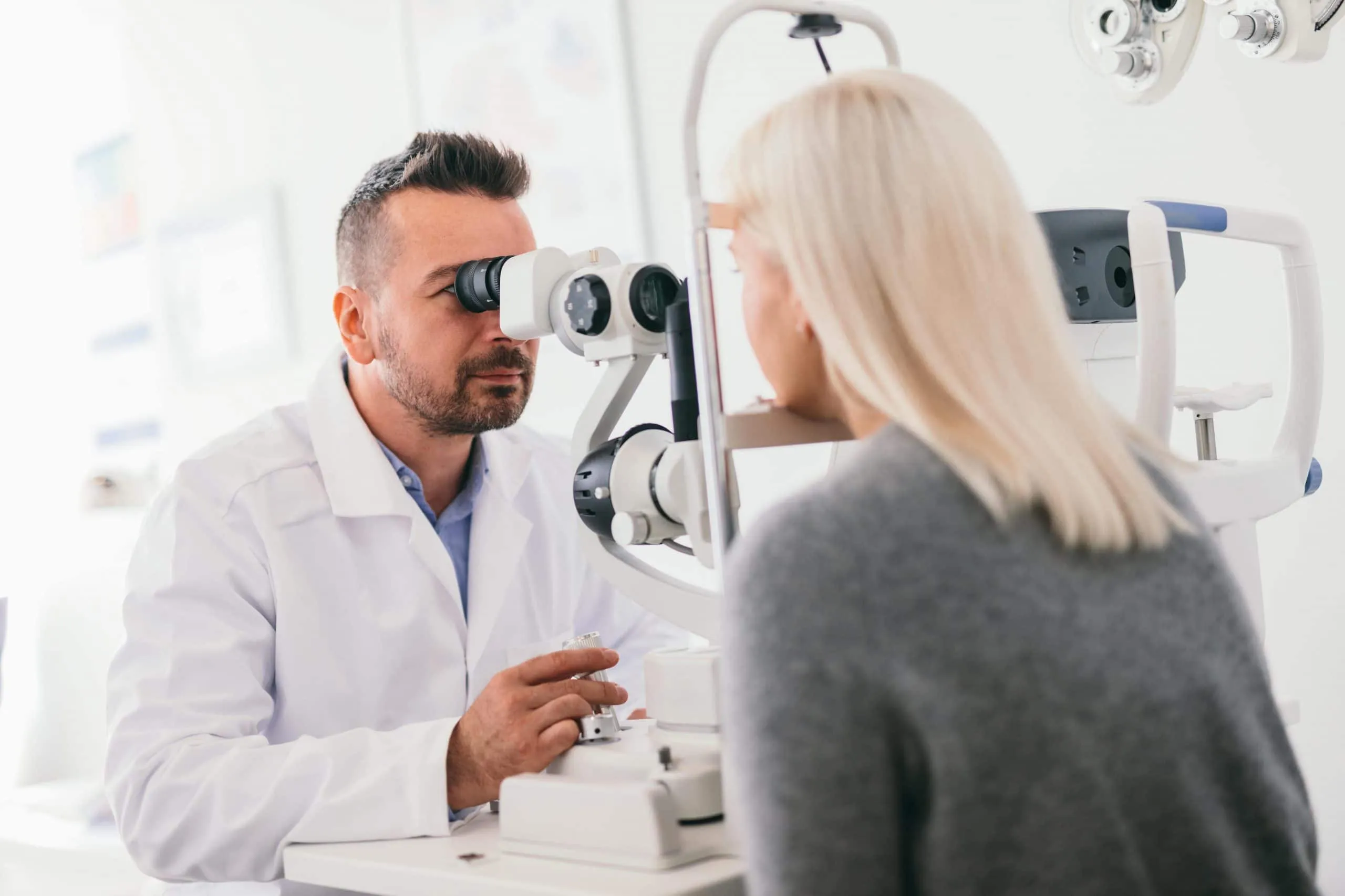 Optometrist med očesnim pregledom stranke na optični napravi